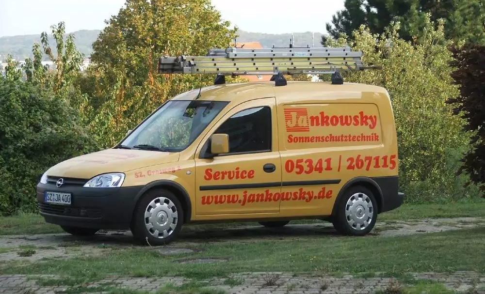 Ein gelber Kastenwagen mit roten Aufdrucken der Jankowsky GmbH und einer Leiter auf dem Dach.