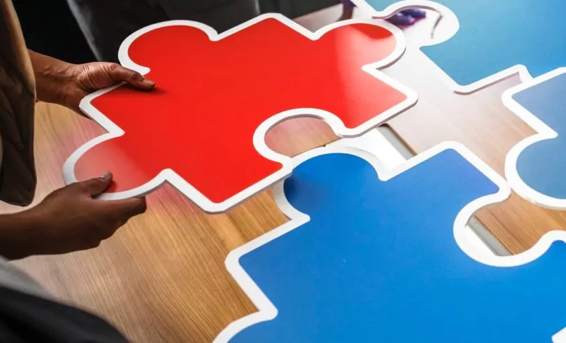 Eine Person fügt ein großes rotes Puzzlestück mit blauen Stücken zusammen.