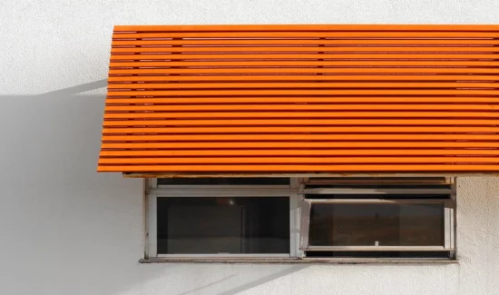 Ein Vordach in kräftigem Orange über einem Fenster in einer weißen Hauswand.
