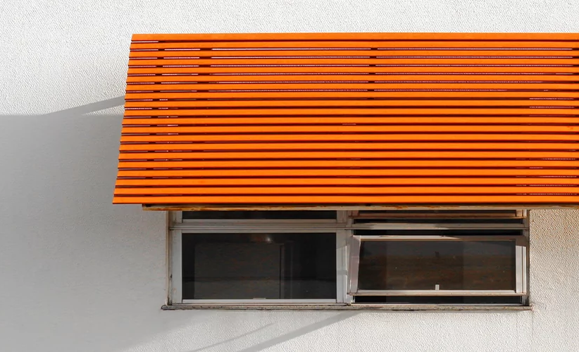 Ein Vordach in kräftigem Orange über einem Fenster in einer weißen Hauswand.